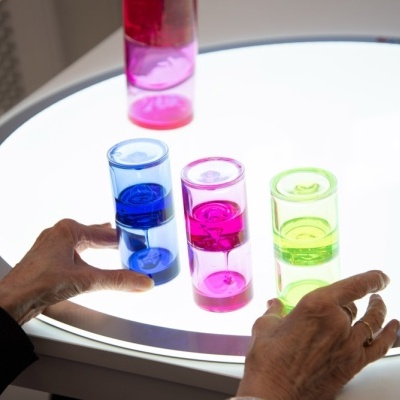 Três copos coloridos sobre mesa iluminada com mãos a segurar