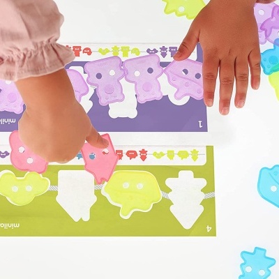 Mãos infantis organizam peças coloridas em formas variadas sobre bases numeradas.