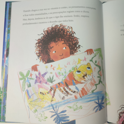 Ilustração de criança segurando desenho colorido de tigre em livro infantil em português