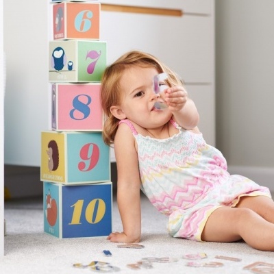Menina criança sentada no chão ao lado de cubos coloridos com números e imagens de animais