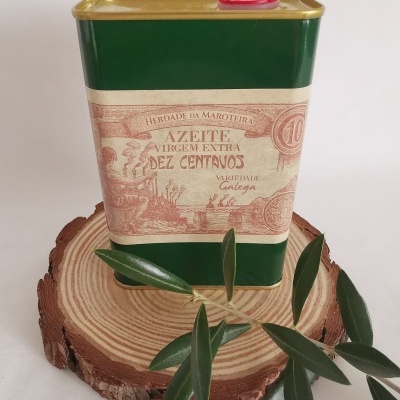 Lata verde de azeite virgem extra com etiqueta bege, apoiada em base de madeira com folhas verdes