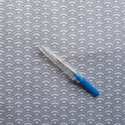 Recortador de unhas transparente com cabo azul sobre superfície cinza com padrão de ondas