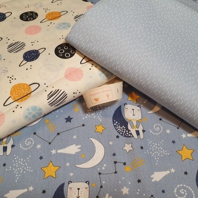 Três tecidos coloridos com padrões de planetas, tecido azul claro com textura branca e tecido azul com ursos e estrelas.