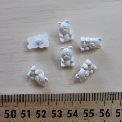 Botões brancos em forma de ursinho junto a régua em superfície de madeira clara