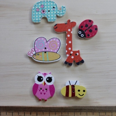 Ímanes decorativos de madeira em formas de animais coloridos sobre uma superfície clara com régua ao lado