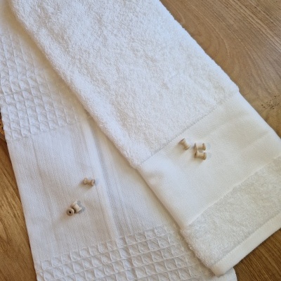 Duas toalhas brancas com texturas diferentes e pequenos objetos de madeira em cima, sobre mesa de madeira