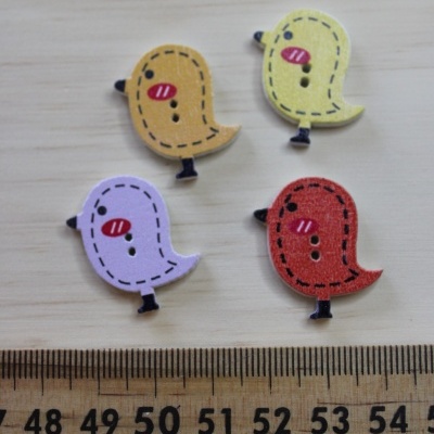 Botões em forma de pássaros coloridos sobre superfície de madeira com régua