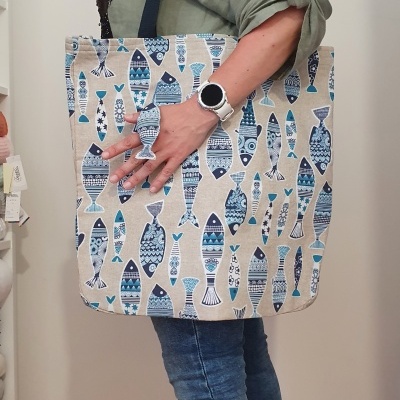 Mala de tecido bege com padrão de peixes azuis, segurada por uma pessoa