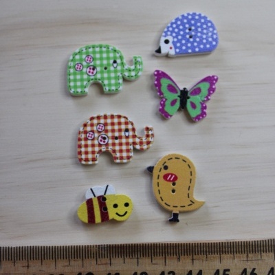 Botões decorativos em forma de animais coloridos sobre superfície clara com régua ao lado