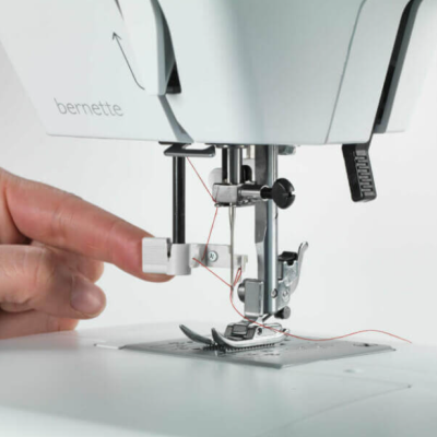Máquina de costura branca bernette com linha vermelha e mão ajustando componente próximo à agulha