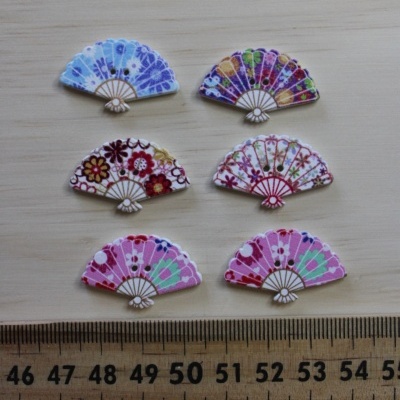 Seis botões pequenos em forma de leque com estampas florais coloridas sobre superfície de madeira clara e régua ao lado.