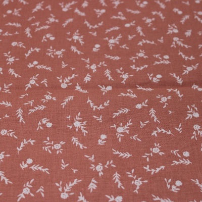 Tecido cor de ferrugem com padrão floral branco pequeno repetido uniformemente