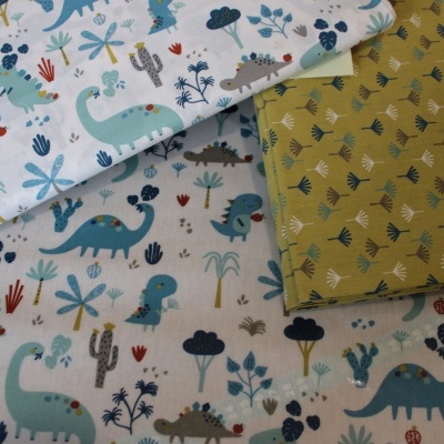 Tecidos infantis com padrões de dinossauros e plantas em cores azul, verde, cinzento e mostarda