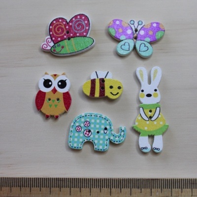 Botões decorativos de madeira com desenhos de animais e insetos coloridos junto a uma régua.