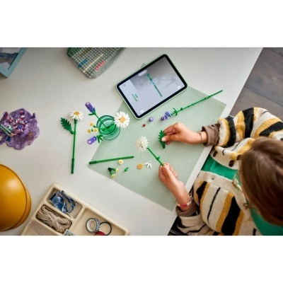 Criança a montar flores de brinquedo em mesa com tablet e materiais de artesanato