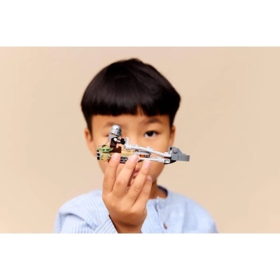 Criança segura brinquedo de construção LEGO em forma de nave espacial cinzenta com mini figuras.