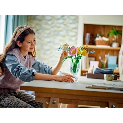 Vaso de vidro com flores coloridas numa mesa de madeira com menina ao lado