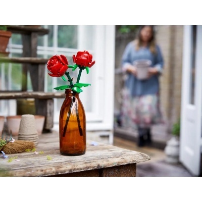 Garrafa de vidro âmbar com flores vermelhas de plástico numa mesa de madeira rústica