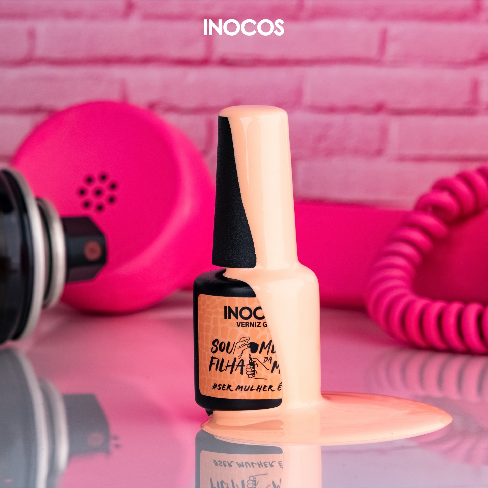 Verniz Gel Inocos – 319 - Sou Mesmo Filha Da Mãe Verniz gel cor de pêssego da INOCOS derramado ao lado do frasco com fundo rosa e acessórios de manicure.