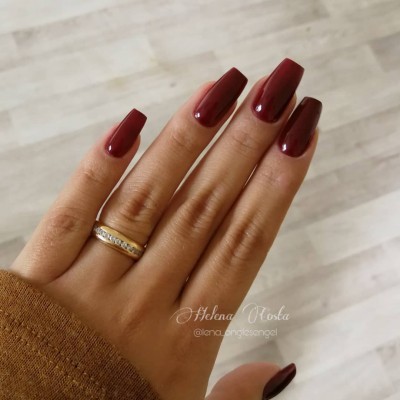 Mão feminina com unhas castanho escuro e anel dourado com pedras