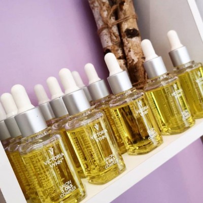 Frascos de óleo amarelo com conta-gotas numa prateleira branca e parede lilás