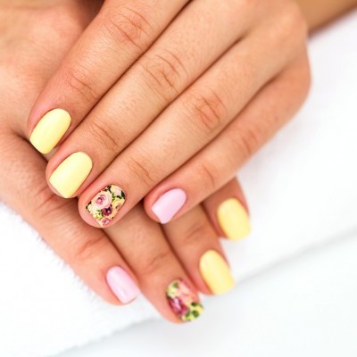 Unhas com verniz amarelo, rosa e design floral sobre toalha branca