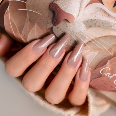 Mão com unhas de verniz nude brilhante segurando artigo decorativo de gato.