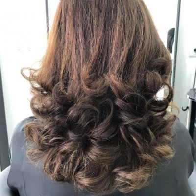 Parte de trás do cabelo castanho claro com cachos definidos, capa preta de cabeleireiro