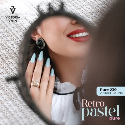 Mulher com unhas azuis pastel, anel dourado, brincos pretos, chapéu branco e batom vermelho refletida em espelho redondo