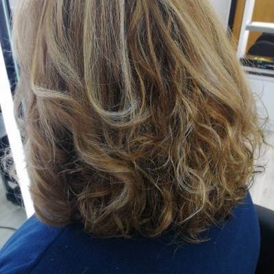 Cabelo ondulado com cores castanho, loiro e reflexos acinzentados vista do atrás num ambiente interior