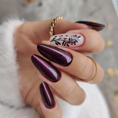 Mão com unhas pintadas de verniz bordeaux e uma unha decorada com padrão de folhas pretas