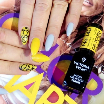 Unhas decoradas amarelas e azul claro segurando verniz gel Victoria Vynn