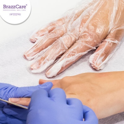 Mãos em procedimento de manicure com luvas e logo BrazzCare