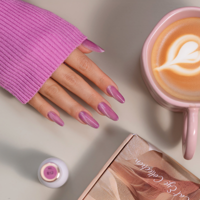 Mão com verniz rosa cintilante próxima a chávena de café rosa e embalagem