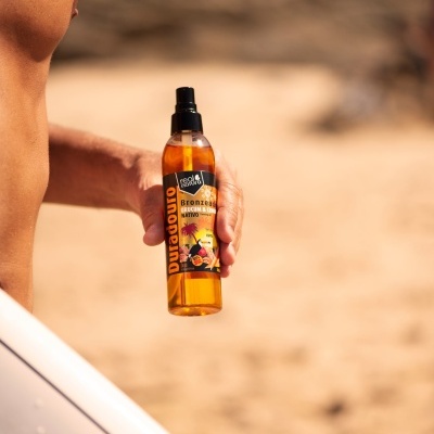 Spray bronzeador em embalagem amarela segurado na praia por mão masculina