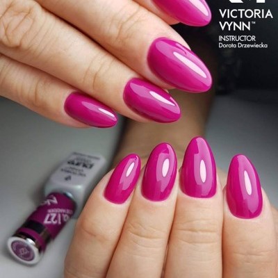 Unhas pintadas de rosa vibrante com frasco de verniz Victoria Vynn ao fundo