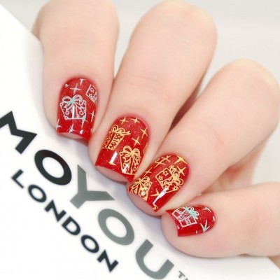 Unhas vermelhas com desenhos de presentes em branco e dourado, estrelas douradas, mão segura embalagem MOYOU LONDON