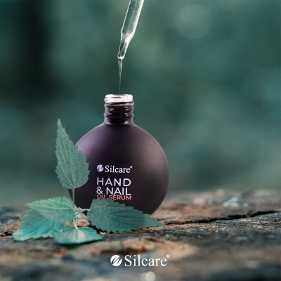 Frasco preto fosco de óleo para mãos e unhas Silcare com conta-gotas, sobre superfície rústica e folhas verdes.