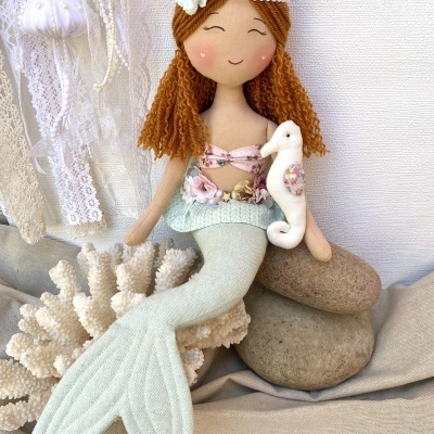 Boneca de sereia de tecido com cavalo-marinho, sentada sobre pedras e coral