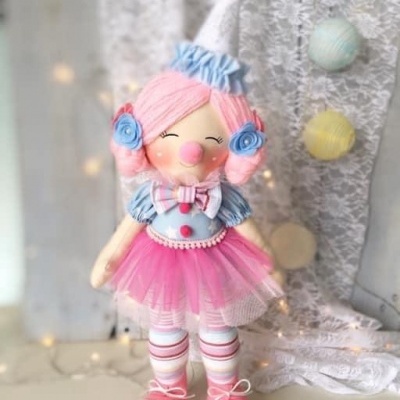 Boneca palhacinha colorida com saia de tule e chapéu em ambiente decorativo com renda e bolas coloridas