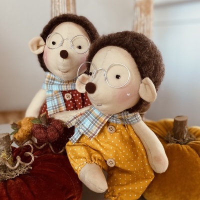 Dois bonecos de tecido com roupa colorida e óculos junto a abóboras de tecido coloridas