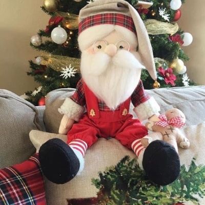 Boneco de Papai Noel sentado em almofada com árvore de Natal ao fundo