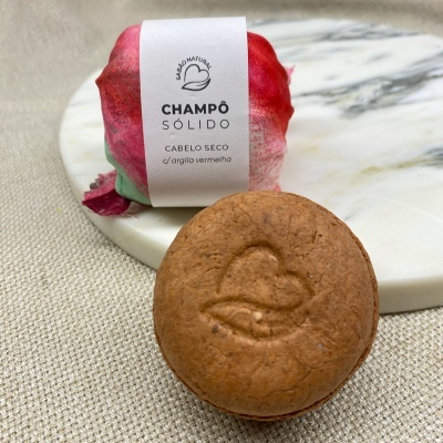 Champô sólido castanho com símbolo em relevo e embalagem branca com texto, sobre base marmoreada e tecido claro