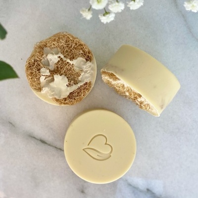 Sabonetes redondos creme com textura esponjosa e detalhe gravado, sobre superfície branca com flores brancas.