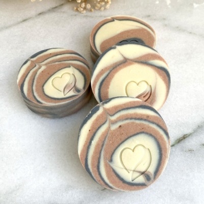 Sabonetes redondos com padrão marmoreado e coração gravado no centro, sobre mármore branco