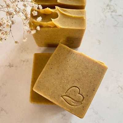 Sabonetes quadrados castanhos claros com textura granulada e marca de coração em relevo, com flores secas brancas ao lado