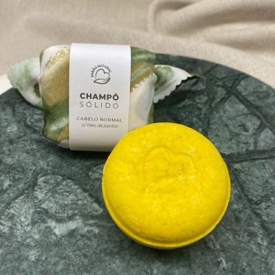 Champô sólido amarelo e embalagem em pano branco verde sobre superfície marmoreada verde