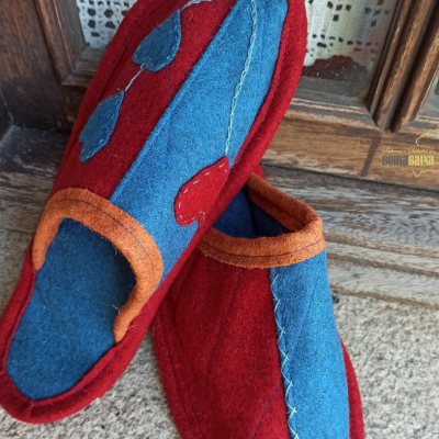 Chinelos de tecido coloridos vermelho, azul e castanho colocados sobre chão de pedra e madeira.