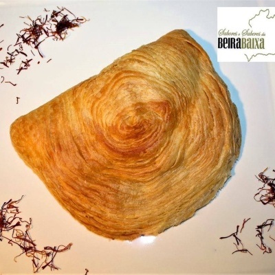 Pastelaria folhada dourada em prato branco com fios marrons e logótipo Sabores e Saberes da Beira Baixa