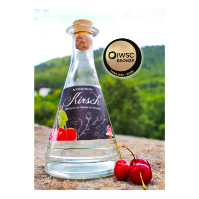 Garrafão de aguardente Kirsch com etiqueta preta, cerejas ao lado e selo IWSC Bronze.